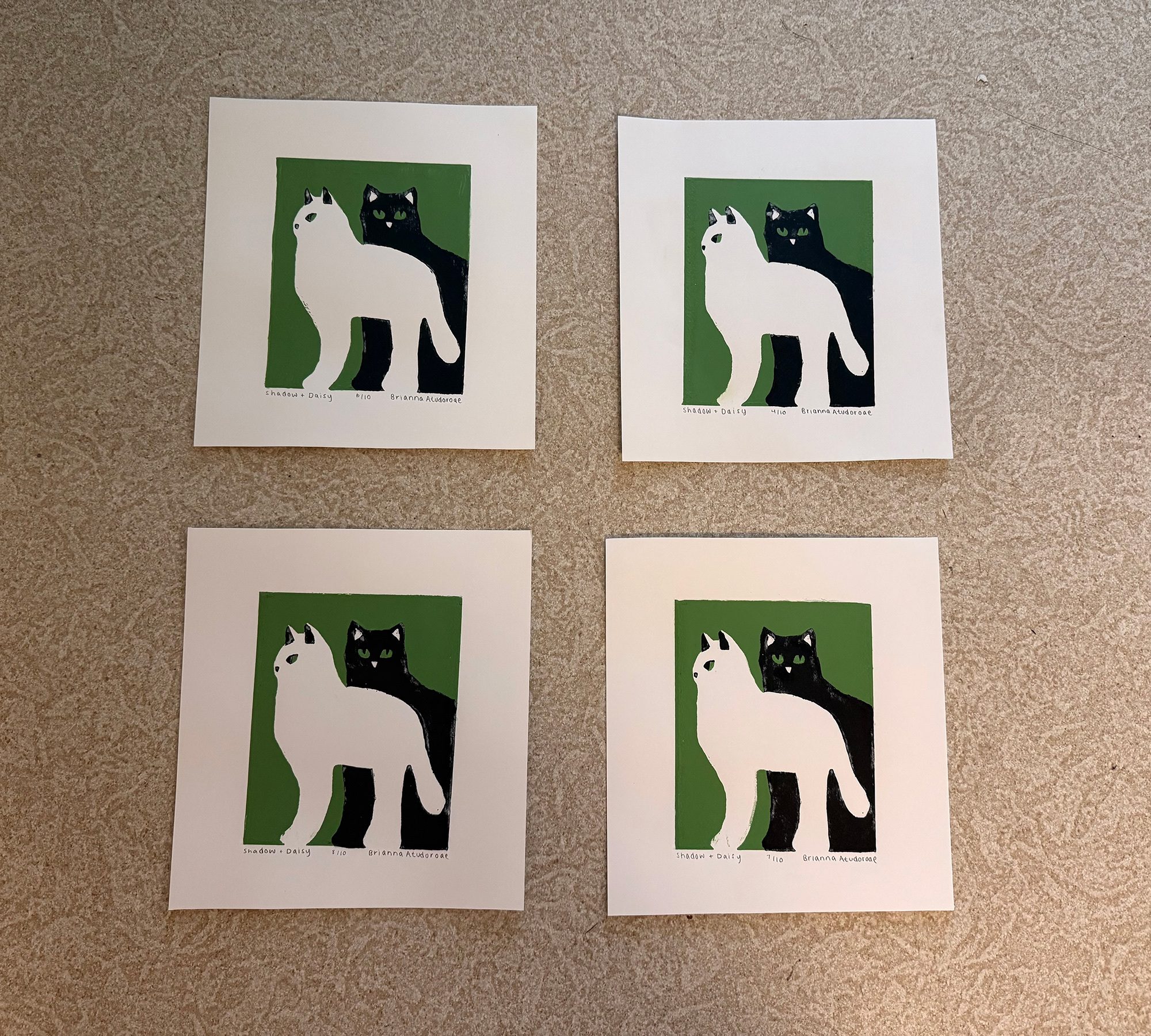 Shadow + Daisy screen prints of a white cat and a black cat on a green background
